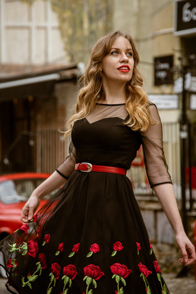 Influencer wears our mesh sleeved swing dress, in black, with embroidered red roses, in front of an old red car