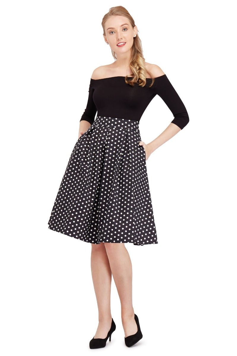 Model wears our high waisted swing skirt, in black, with white polka dots, hands in pockets, front view