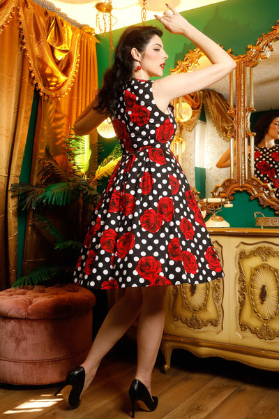 A model wearing an Annie retro dress in black/red roses and white spot print, in a garden