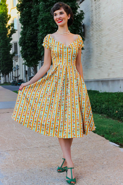 A model wearing a Sicilian Orange Stripe Swing Dress, holds skirt