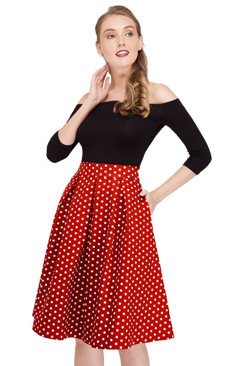 Model wears our black top and high waisted, flared skirt, in red polka dot print, with hands in her pockets, close up view