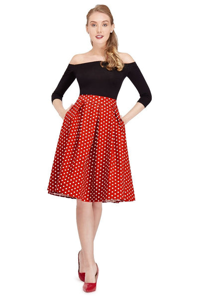Model wears our black top and high waisted, flared skirt, in red polka dot print, with hands in her pockets, front view