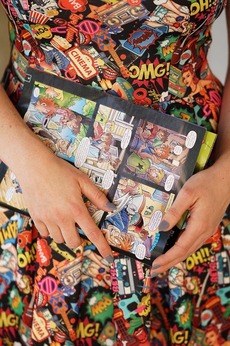 Amanda dress close up, in colourful pop art comic print, whilst holding a comic book